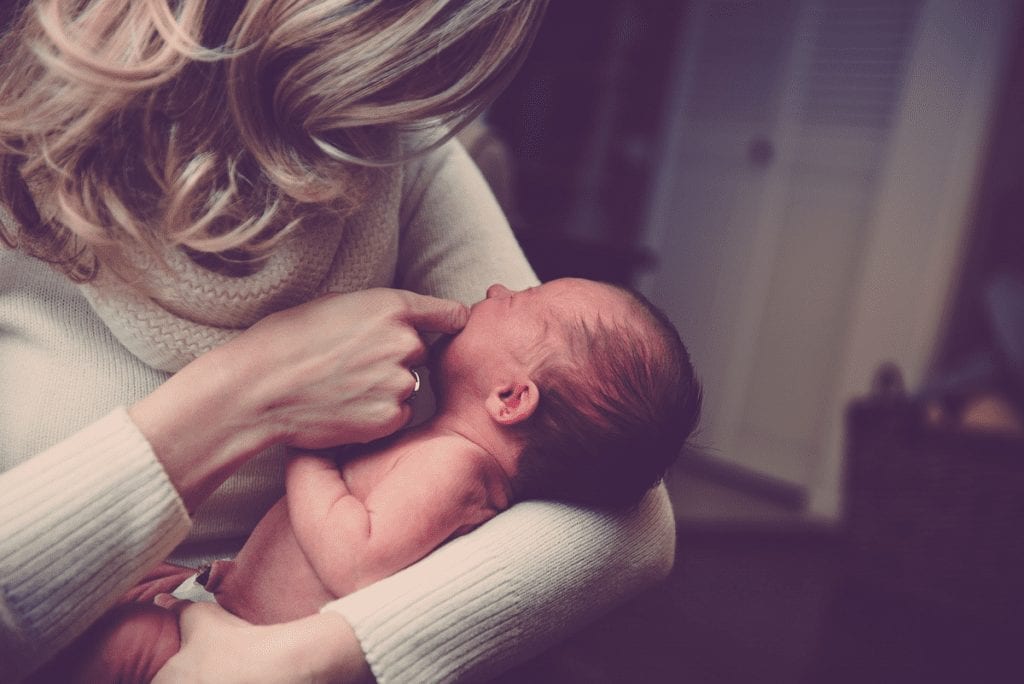 Common Sick Baby Symptoms to Be Watchful For A blond woman in a white sweater holds a newborn baby in her arms